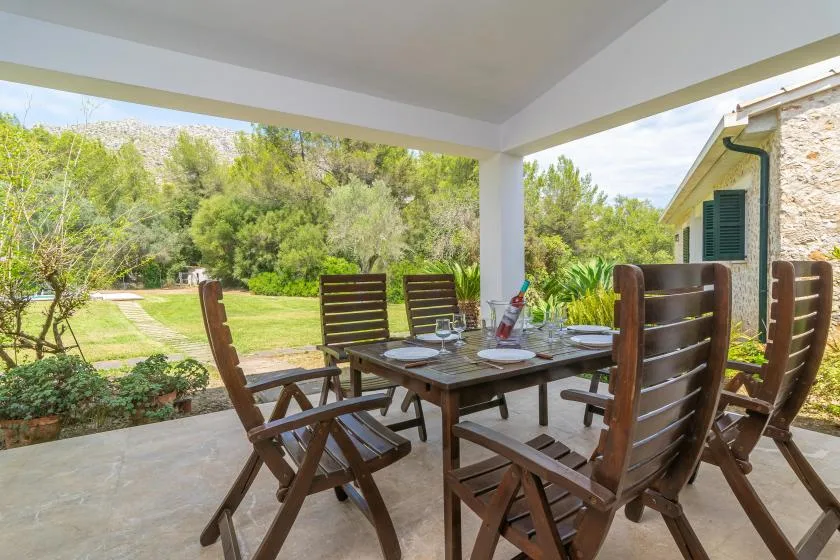 Un comedor en una terraza cubierta con asientos de madera da a un jardín verde.