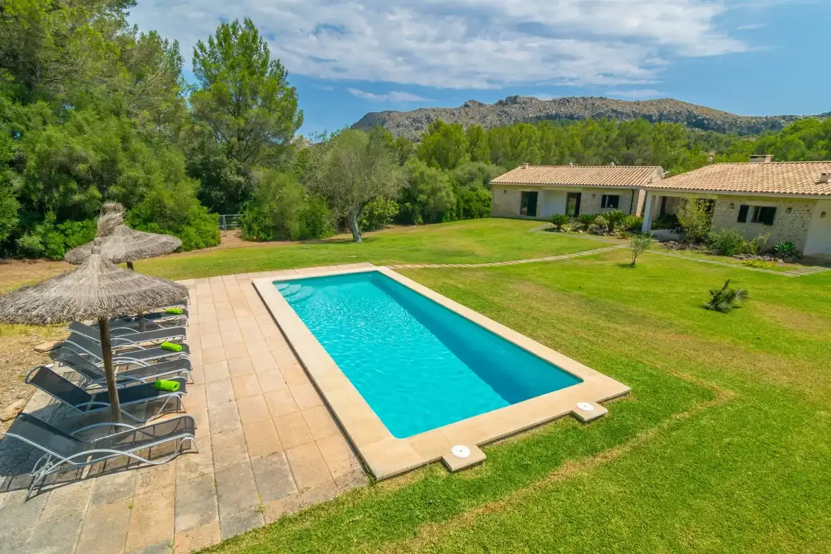 Una piscina al aire libre junto a un césped, con árboles y colinas al fondo.