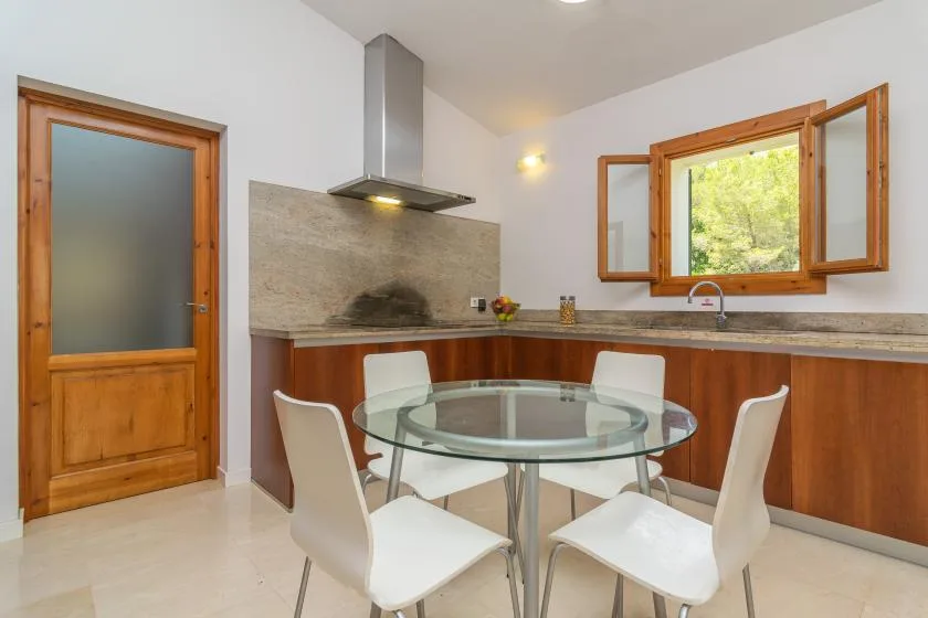 Una cocina y comedor con una mesa redonda de vidrio y gabinetes de madera.
