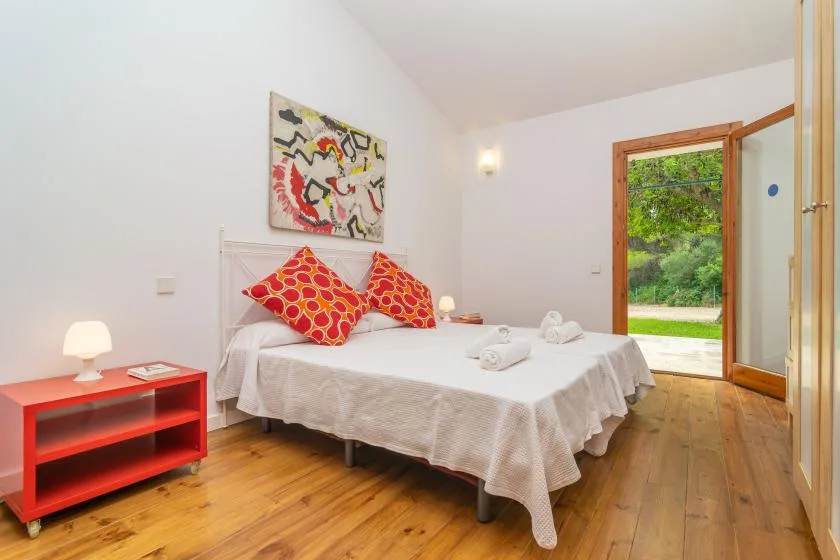 Un dormitorio con una cama bien tendida y una puerta abierta al jardín.
