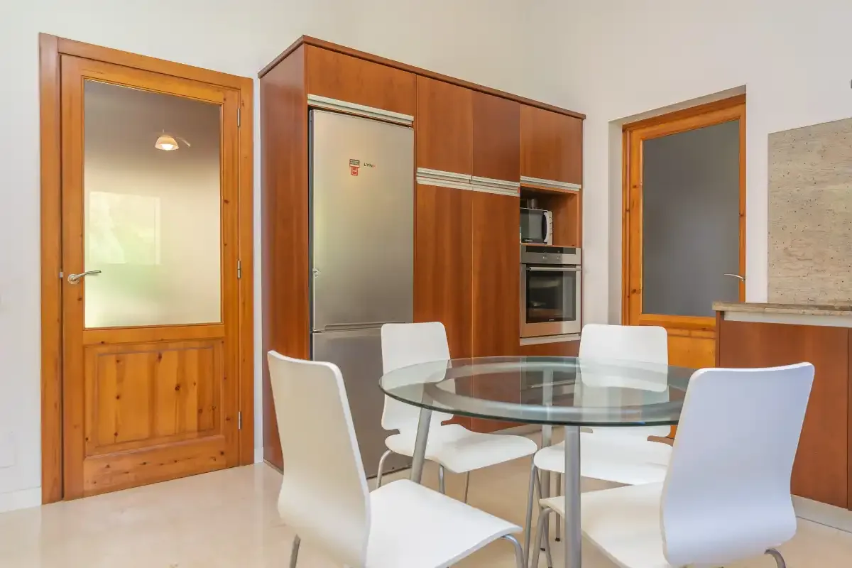Comedor con una mesa de vidrio y asientos blancos junto a la cocina.