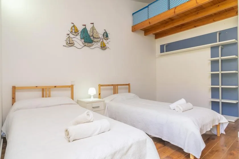 Un dormitorio con dos camas, una pequeña mesita de noche y un altillo de madera.