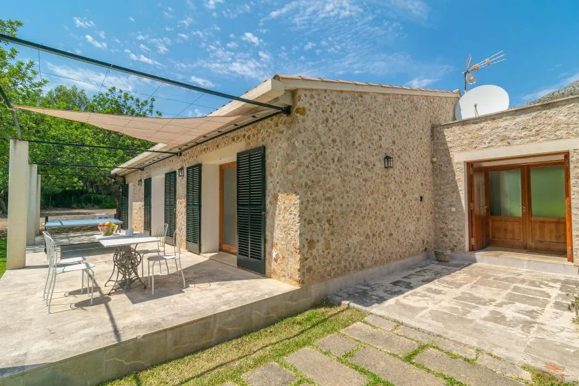 Una casa de piedra se abre a un patio pavimentado con asientos al aire libre bajo un toldo.