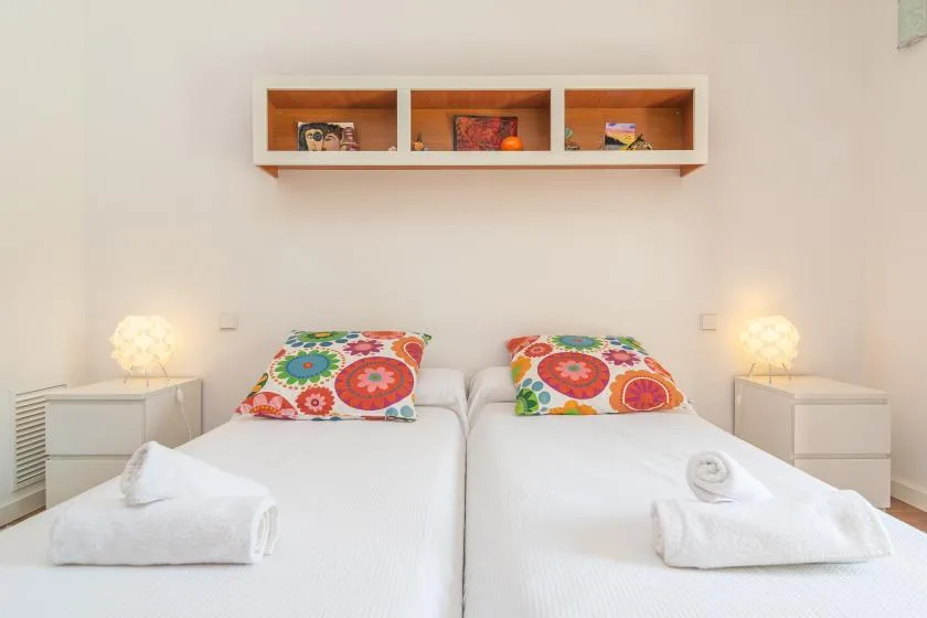 Un dormitorio luminoso con dos camas individuales y almohadas florales de colores.