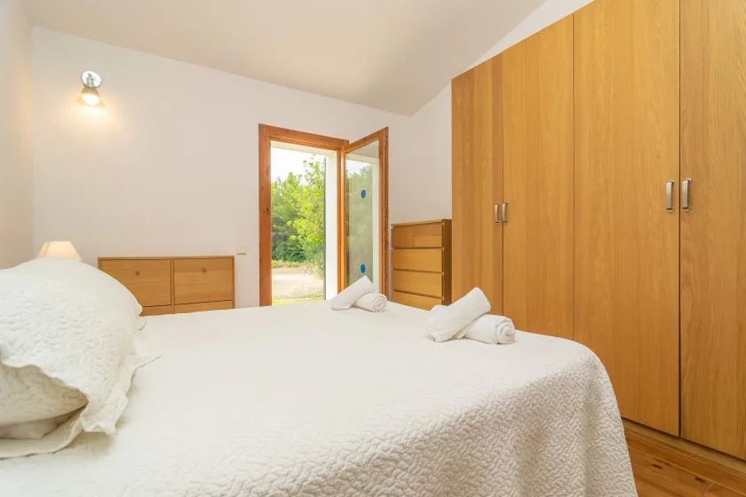 Un dormitorio con una cama, armarios de madera y una puerta abierta hacia la vegetación.