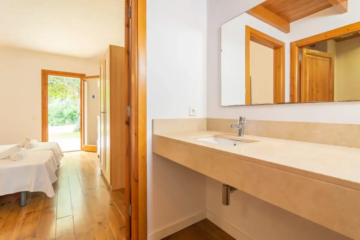 Un lavabo de baño con un espejo amplio da a un dormitorio con una cama.