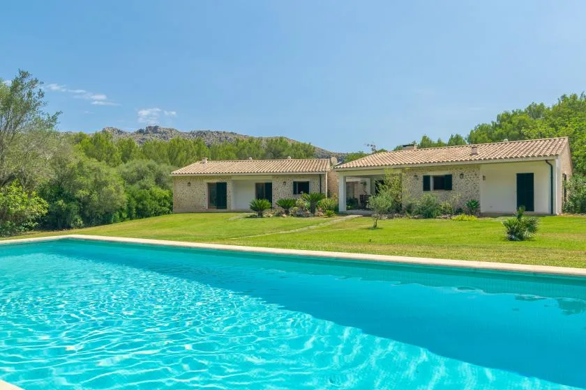 Una piscina frente a una casa de una planta y un césped verde.