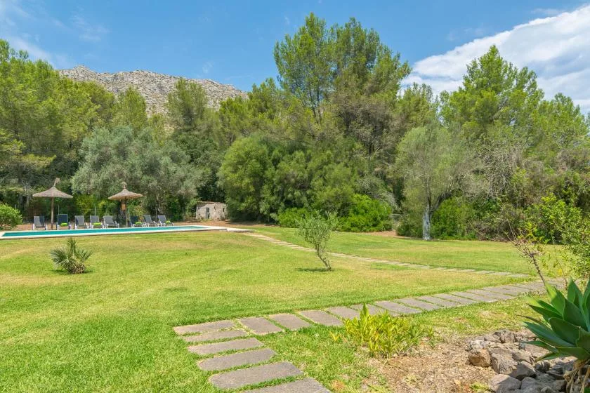 Un jardín ajardinado con césped, losas de paso y una piscina.