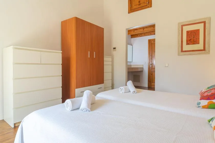 Un dormitorio con camas cubiertas de blanco, un armario de madera y una puerta a otra habitación.