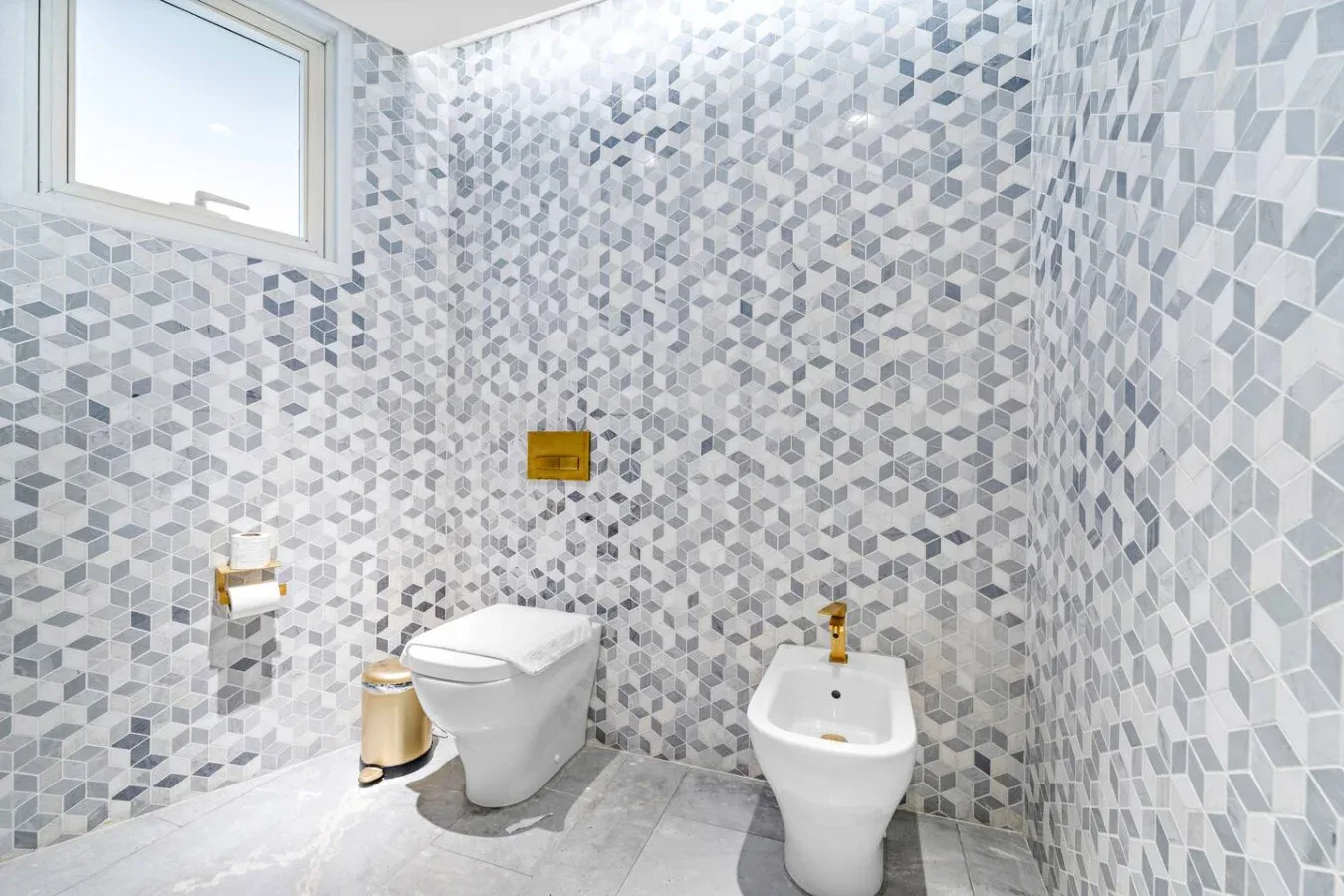 Un baño con azulejos, inodoro, bidé y una ventana pequeña.