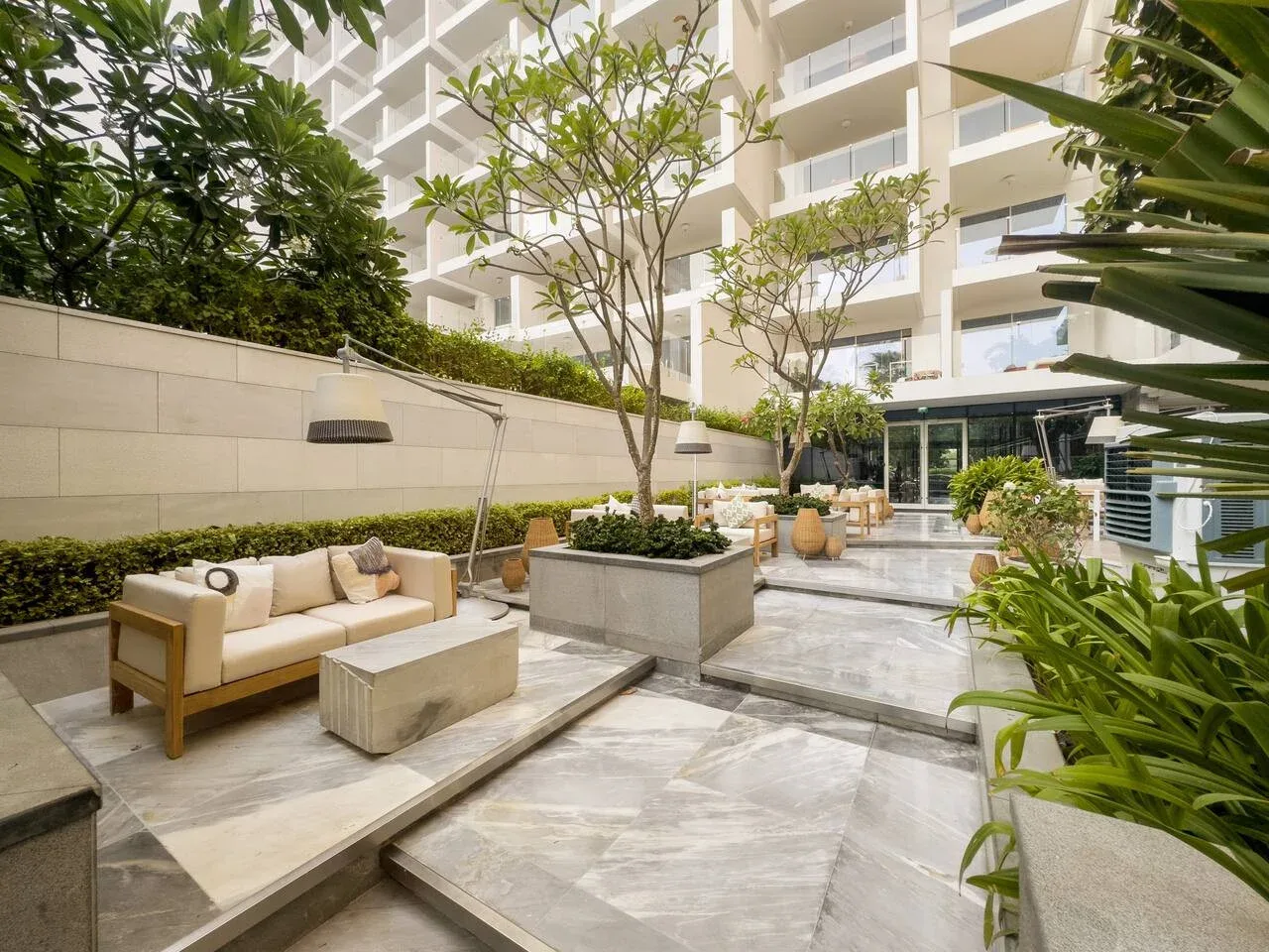 Un patio exterior tiene pavimento escalonado, árboles y una zona de asientos.