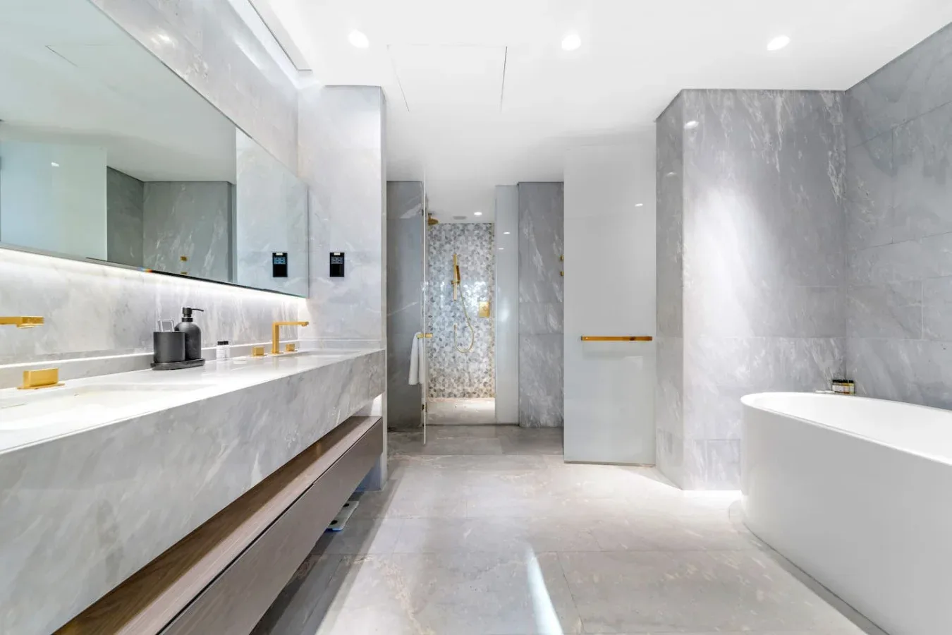 Un baño luminoso de mármol con un tocador largo y una bañera.