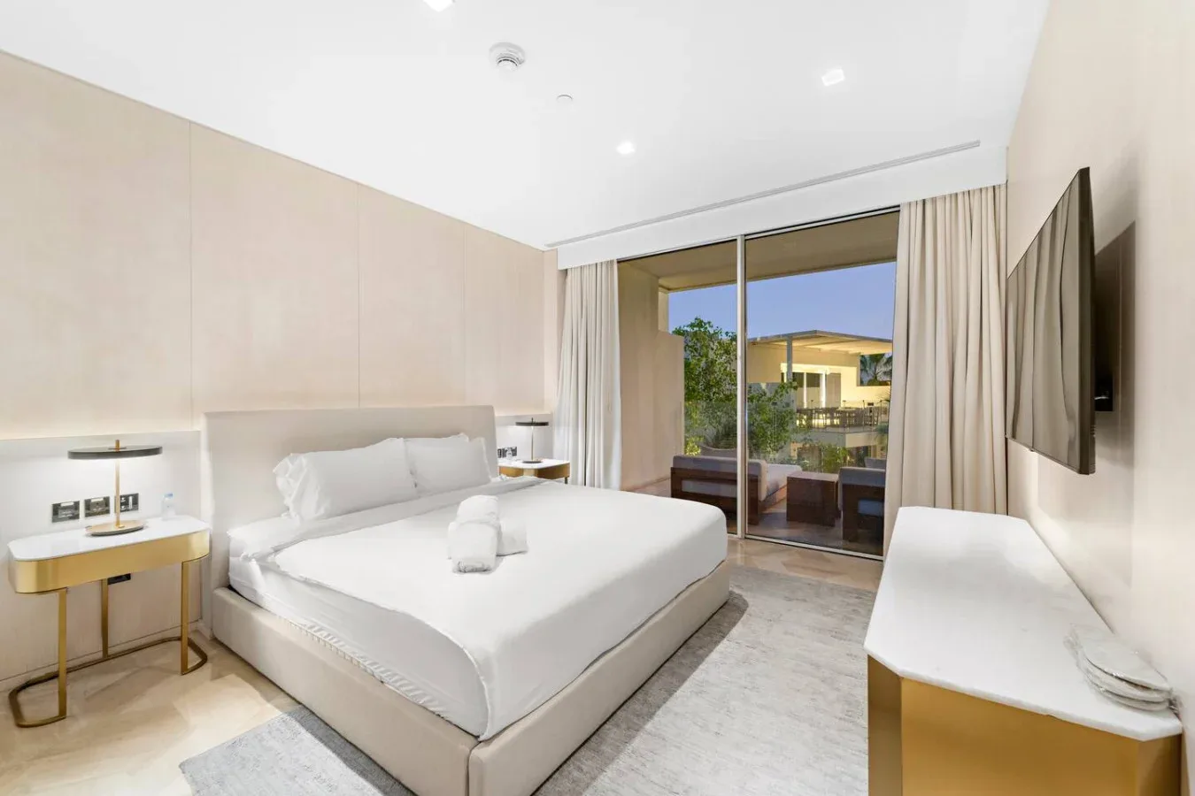Un dormitorio luminoso con una cama blanca y puertas de vidrio que dan a un balcón.