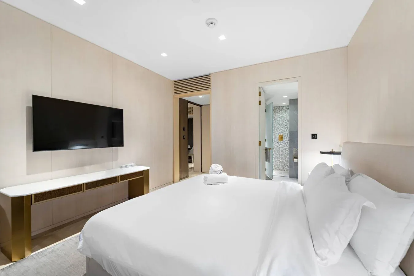 Un dormitorio con una cama grande, un televisor montado en la pared y una puerta abierta al baño.
