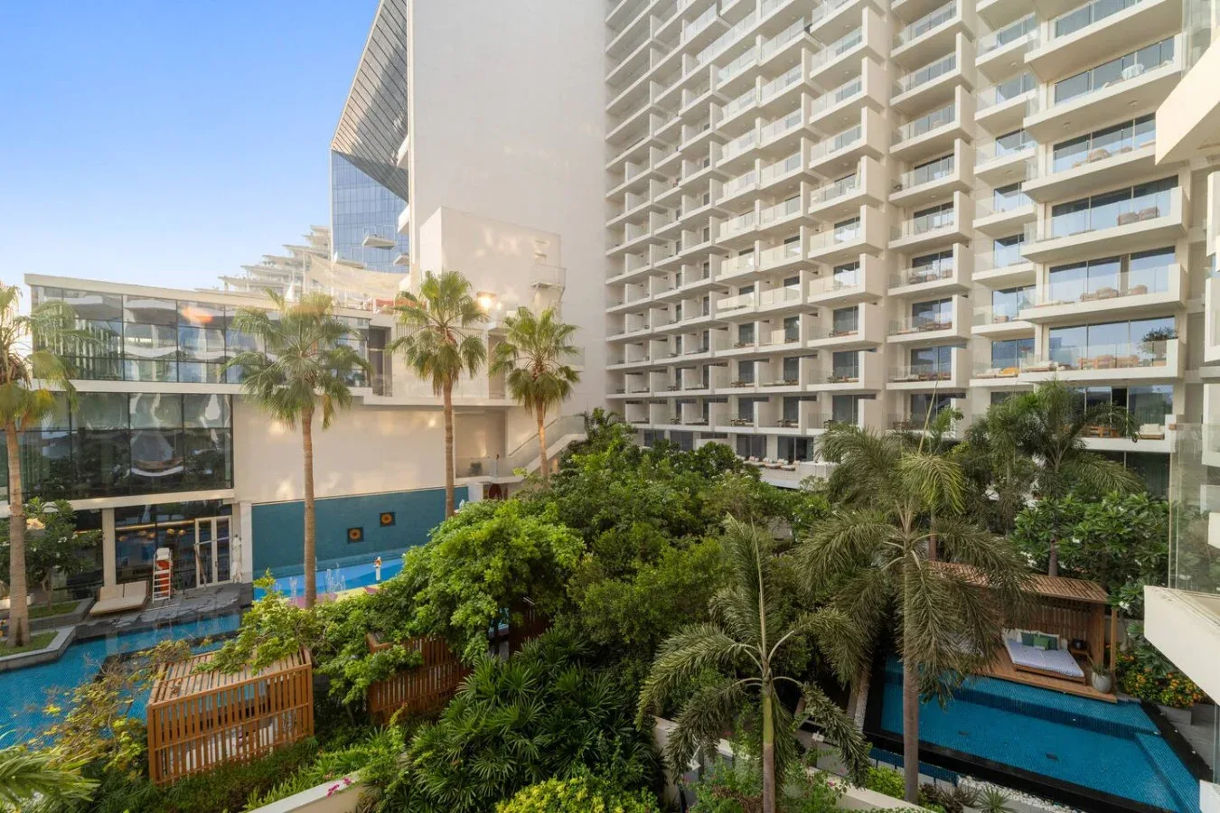 Un patio ajardinado de hotel con palmeras, una piscina y balcones alrededor.