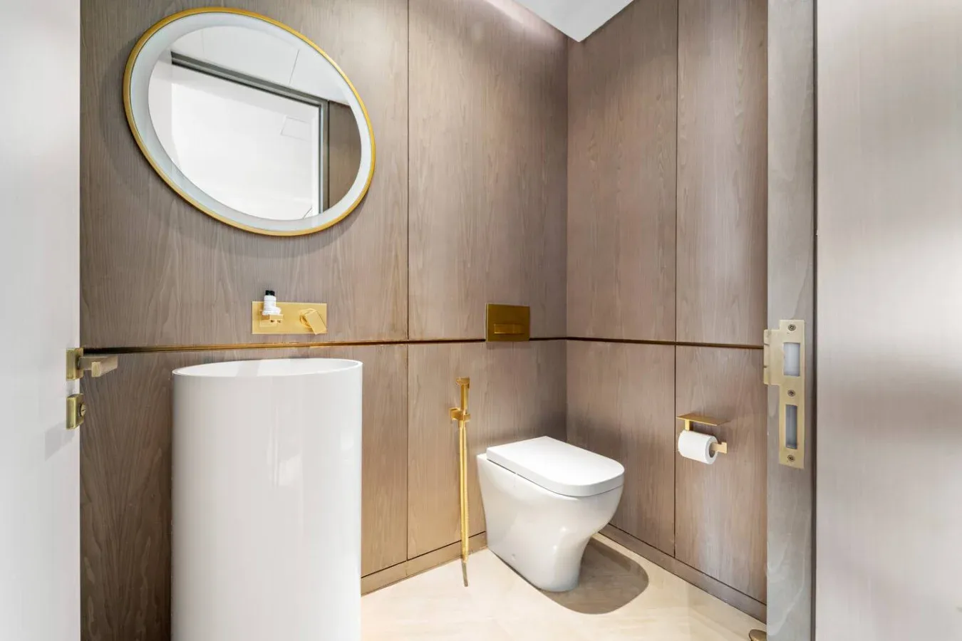 Un baño con inodoro, lavabo de pedestal y espejo ovalado en la pared.