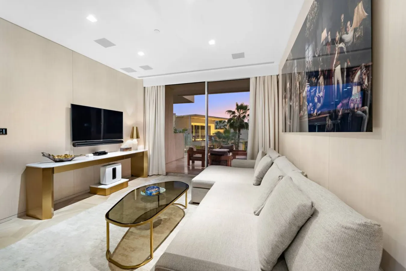 Una sala luminosa con televisor, asientos y puertas de vidrio que dan a un balcón.