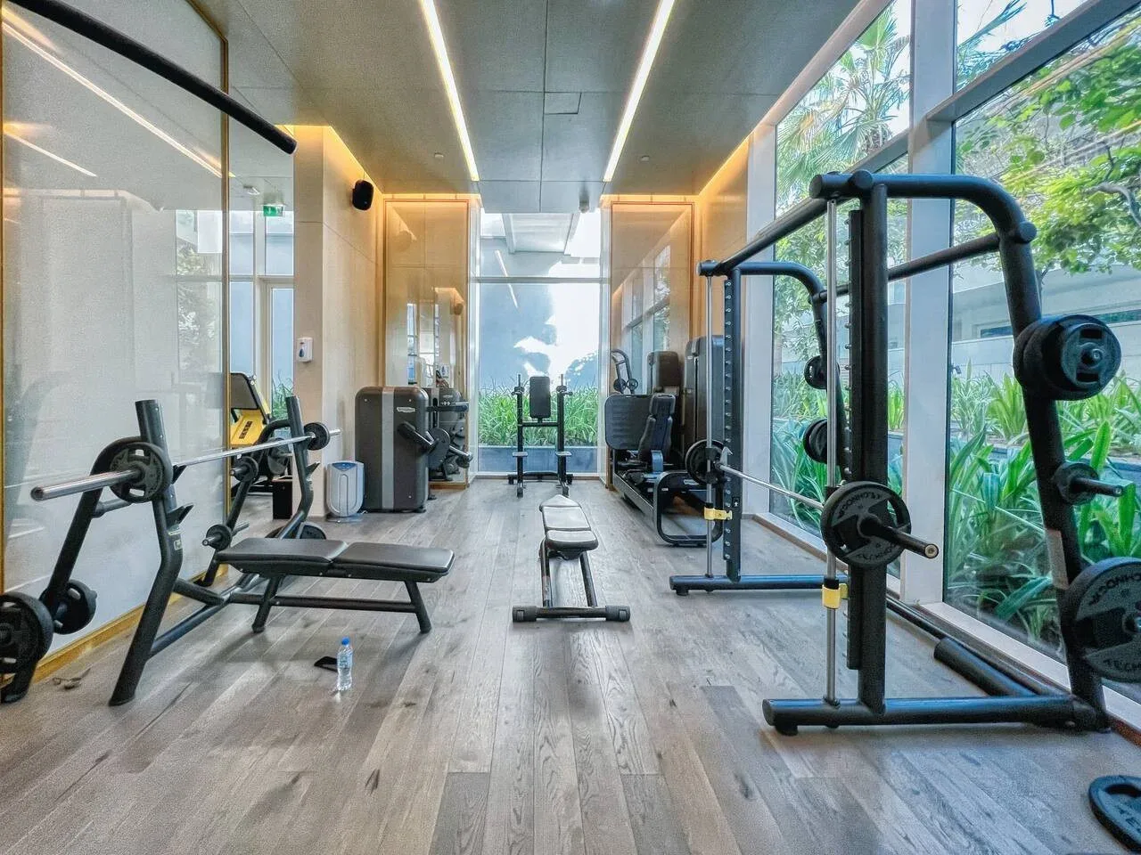 Una sala de ejercicios con máquinas y grandes ventanales frente a la vegetación.