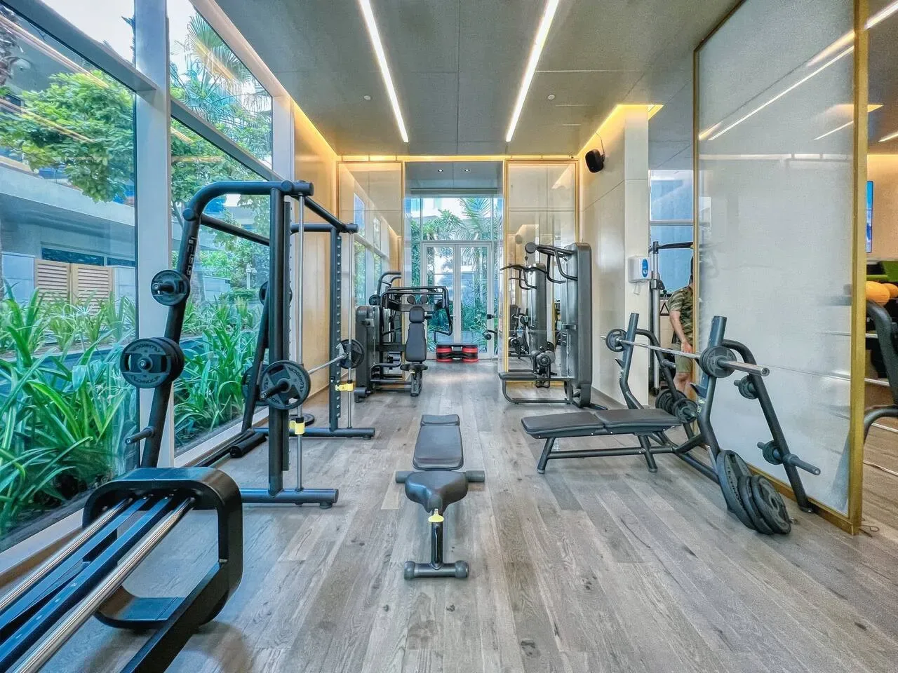 Un gimnasio luminoso con máquinas de ejercicio y grandes ventanales con vistas a la vegetación.