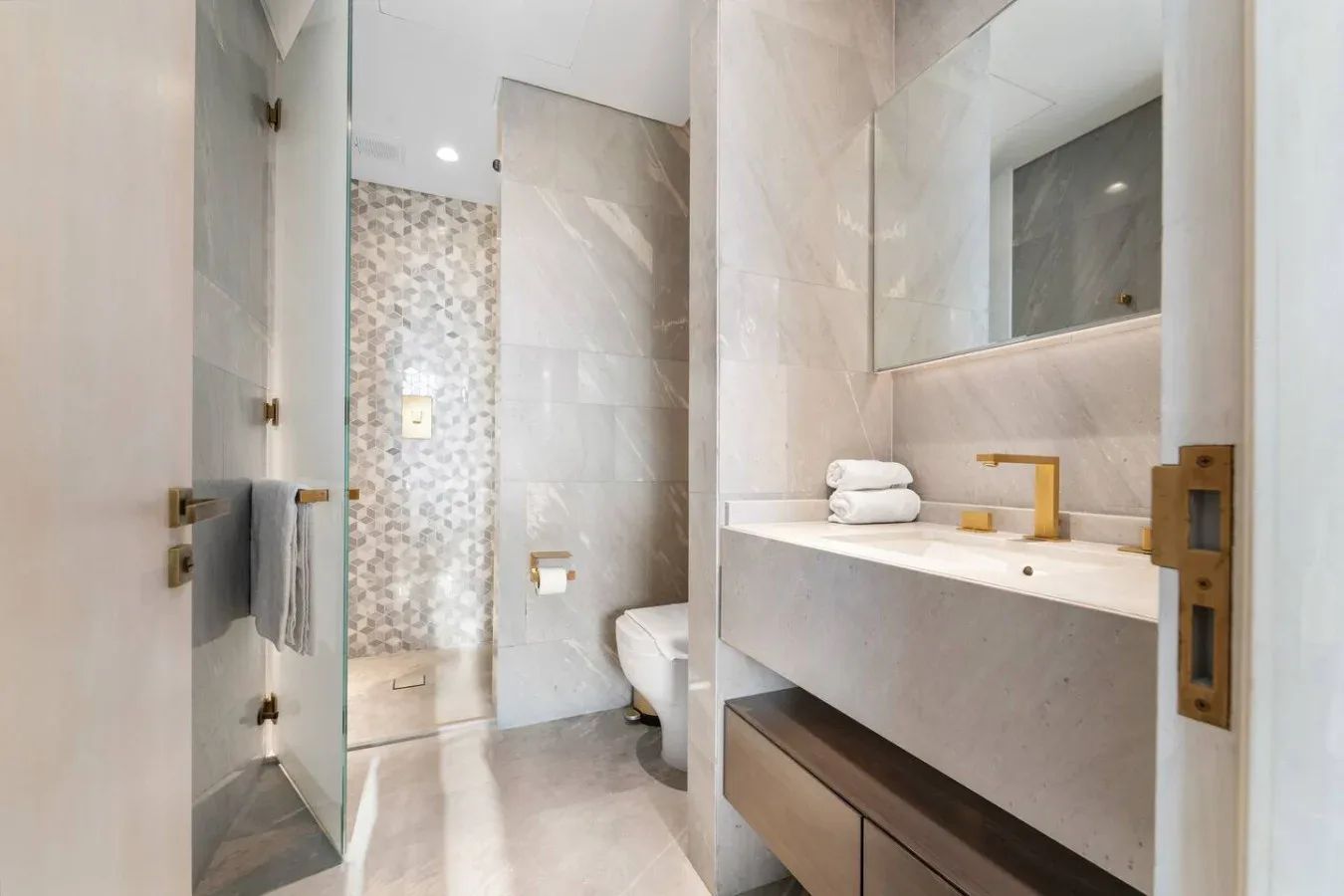 Un baño con azulejos, ducha de vidrio y una encimera larga con lavabo.