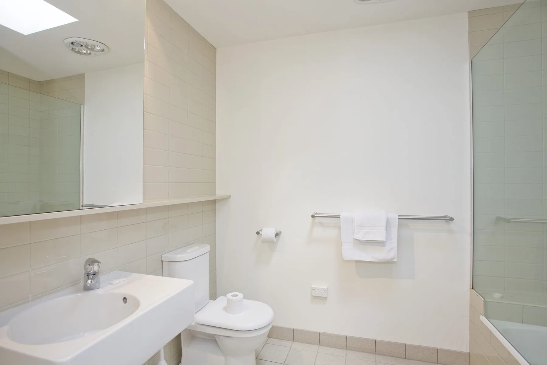 A bright bathroom with a bathtub, toilet, and wall-mounted towel rail.