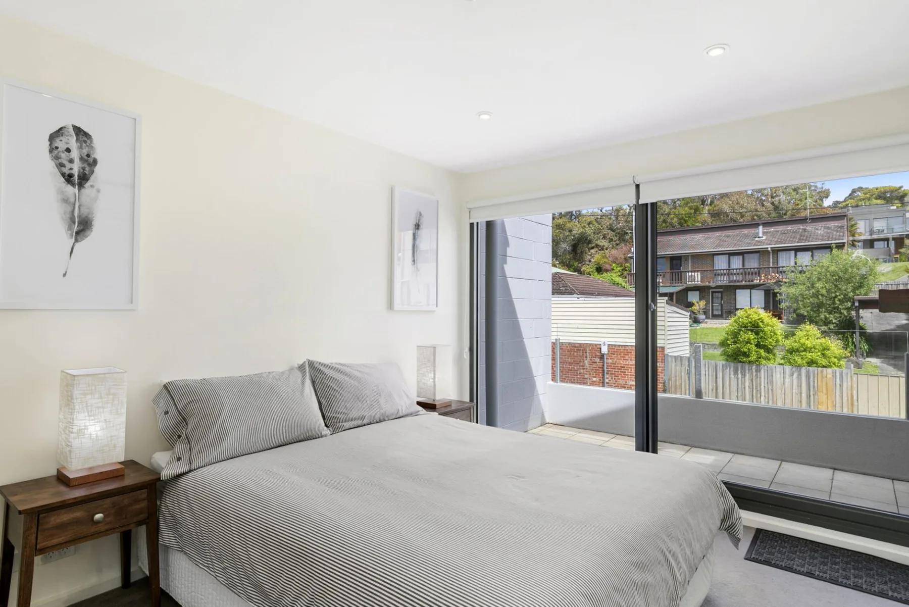A bright bedroom with a large bed beside sliding glass doors opening onto a balcony.