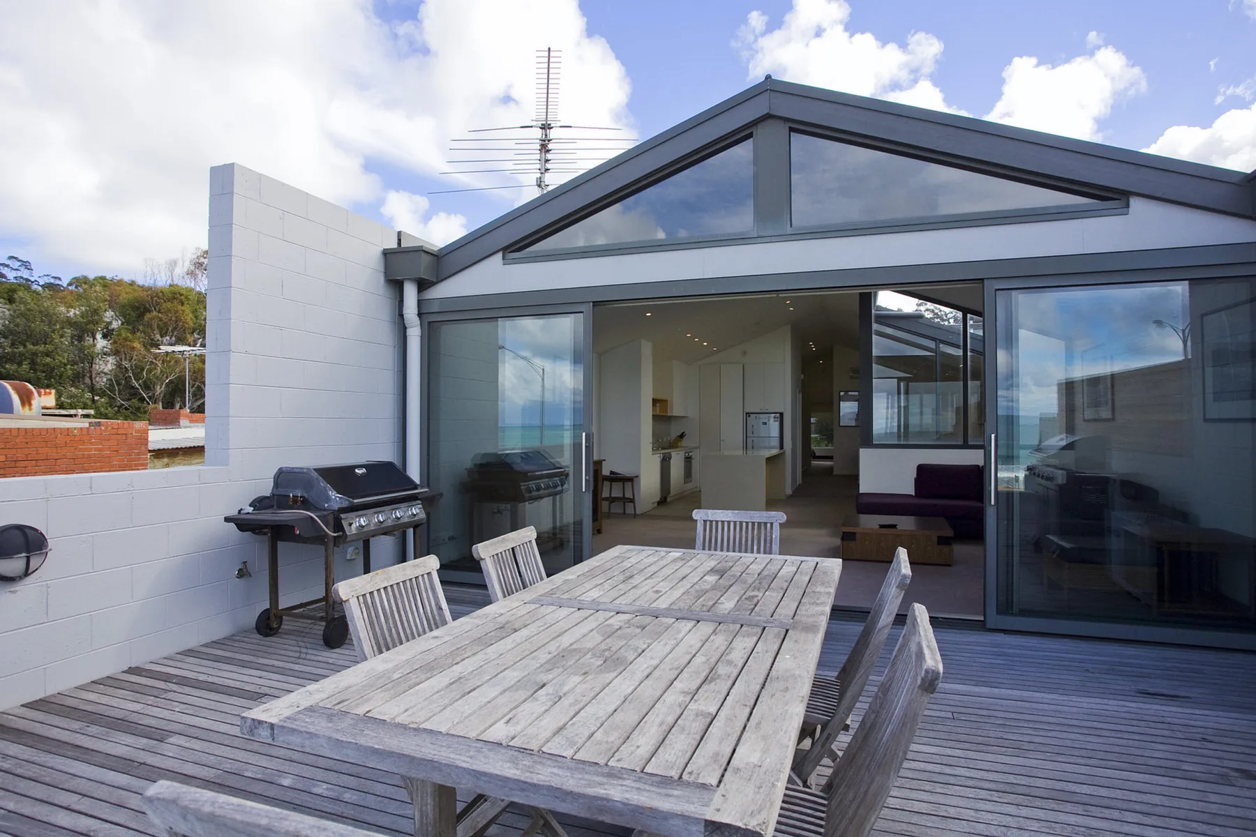 A modern apartment patio with outdoor seating and a barbecue beside large glass doors.