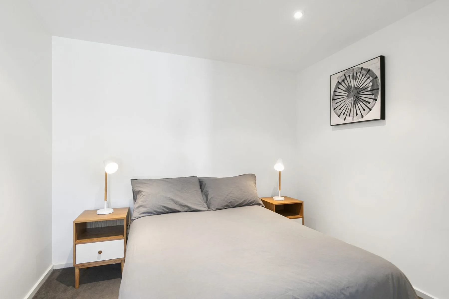 A bedroom with a neatly made bed, bedside tables, and wall art.