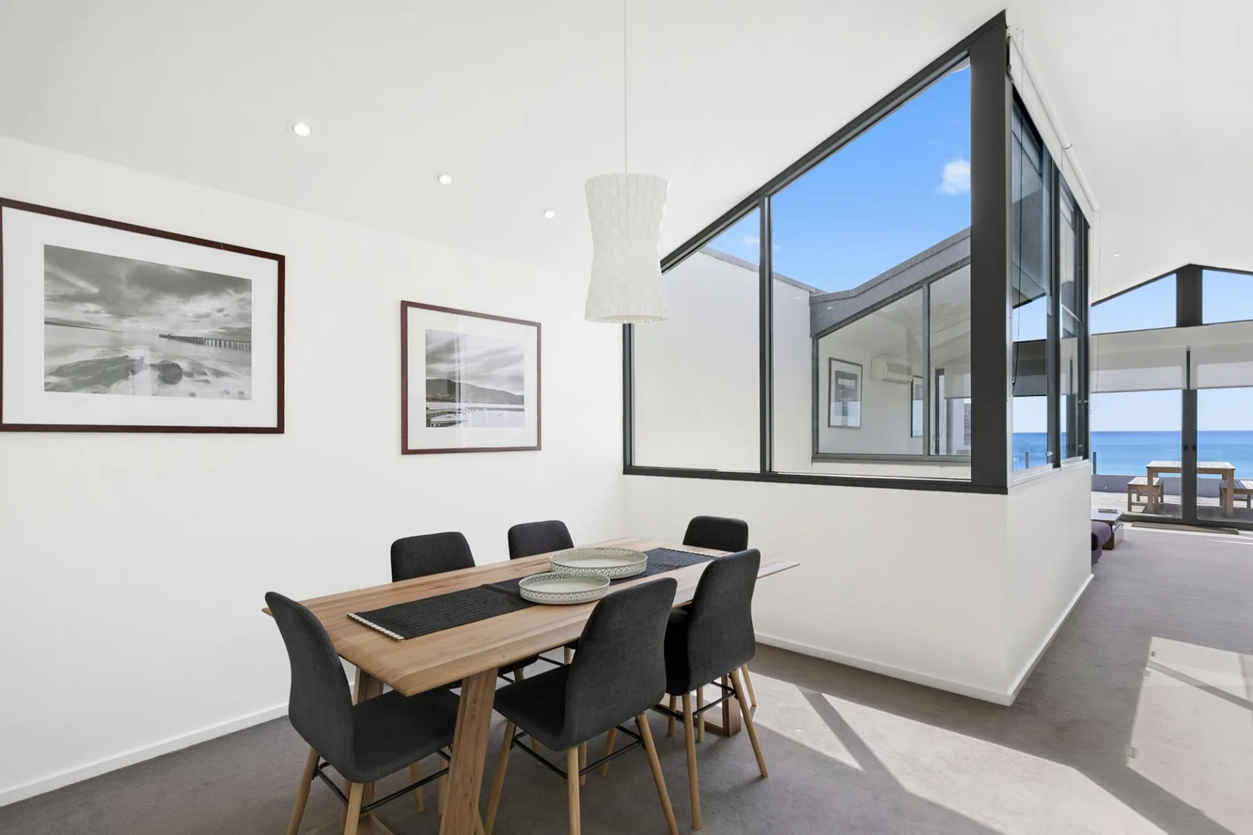 A dining area with a wooden table and seating beside large windows.