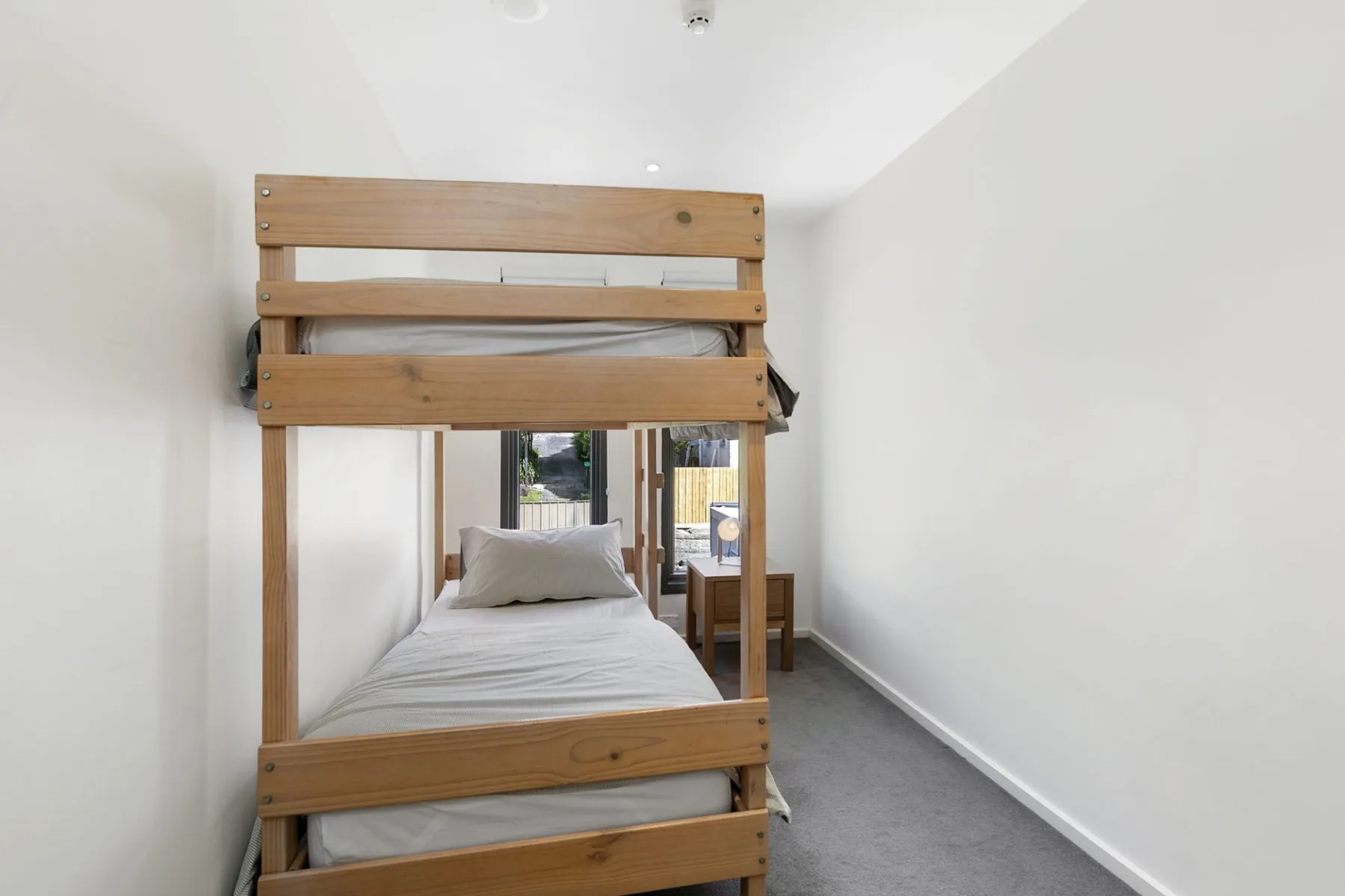 A bedroom with a wooden bunk bed and a narrow window at the far end.