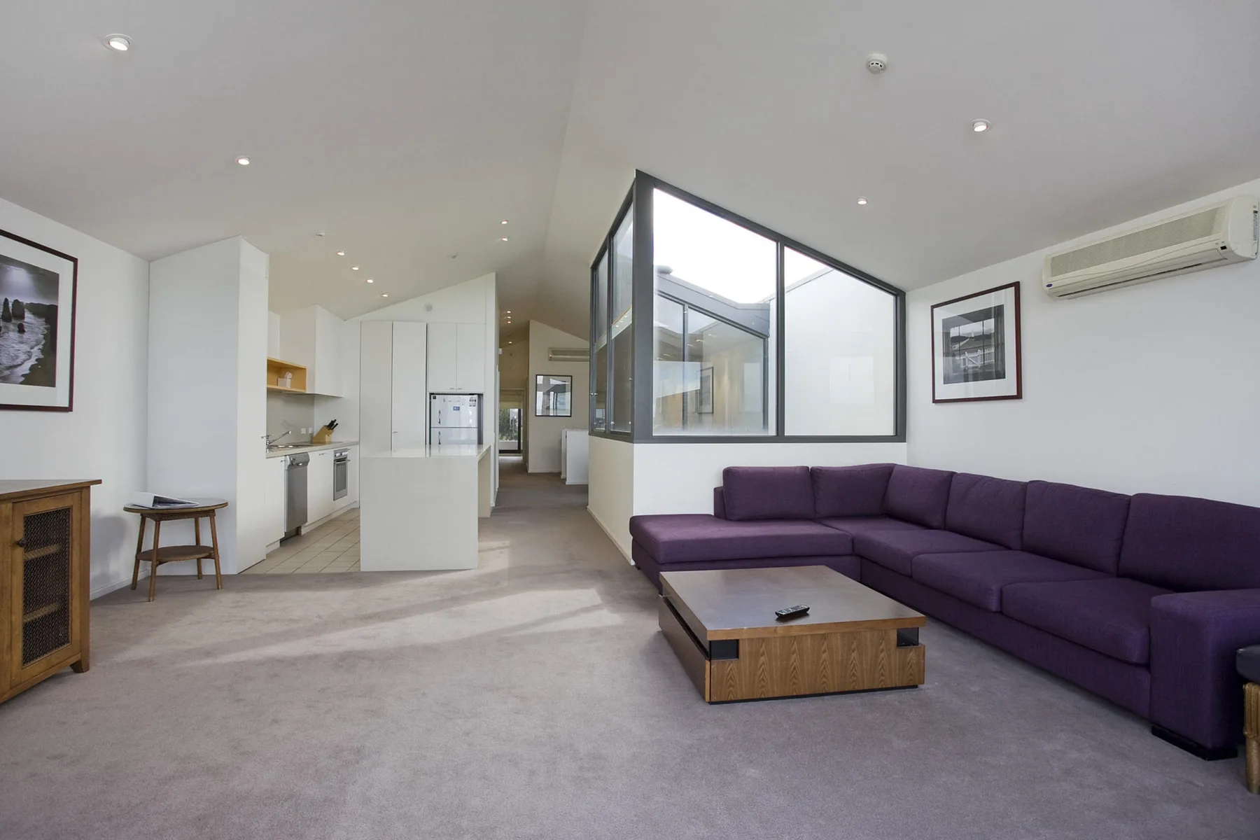 A living room with purple seating and a coffee table beside an open kitchen.