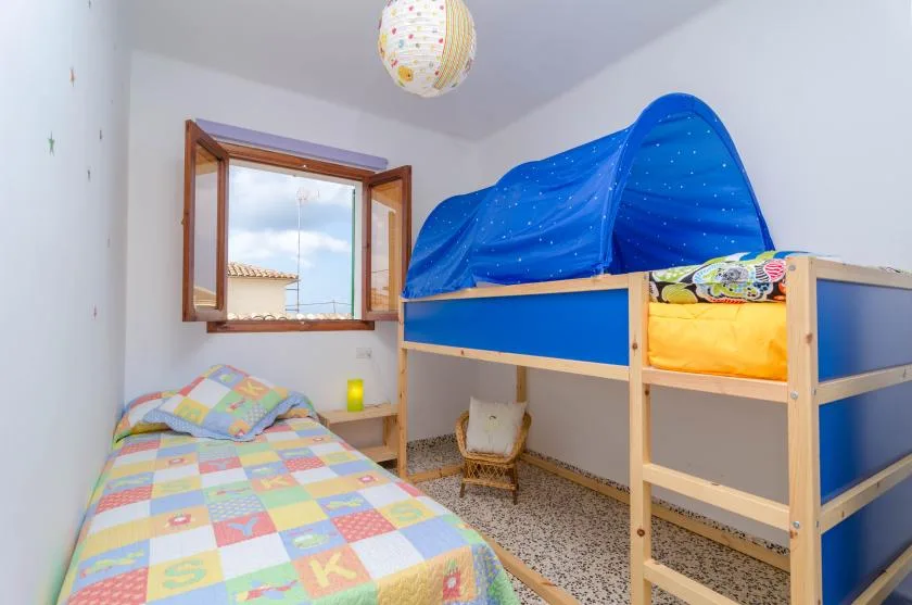 A colorful bedroom with a bed beside a blue bunk bed and an open window.