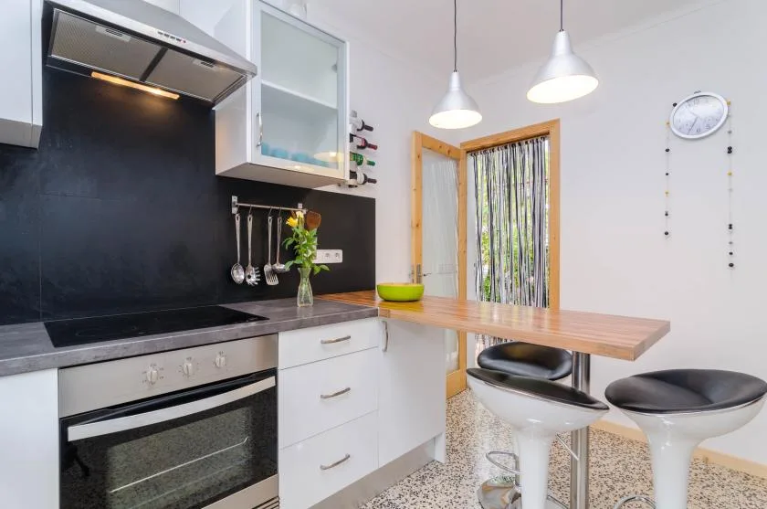 A modern kitchen with a black backsplash, white cabinetry, and a wooden breakfast counter.