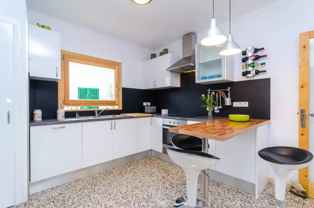 A bright kitchen with white cabinets, a dark backsplash, and a wood counter.