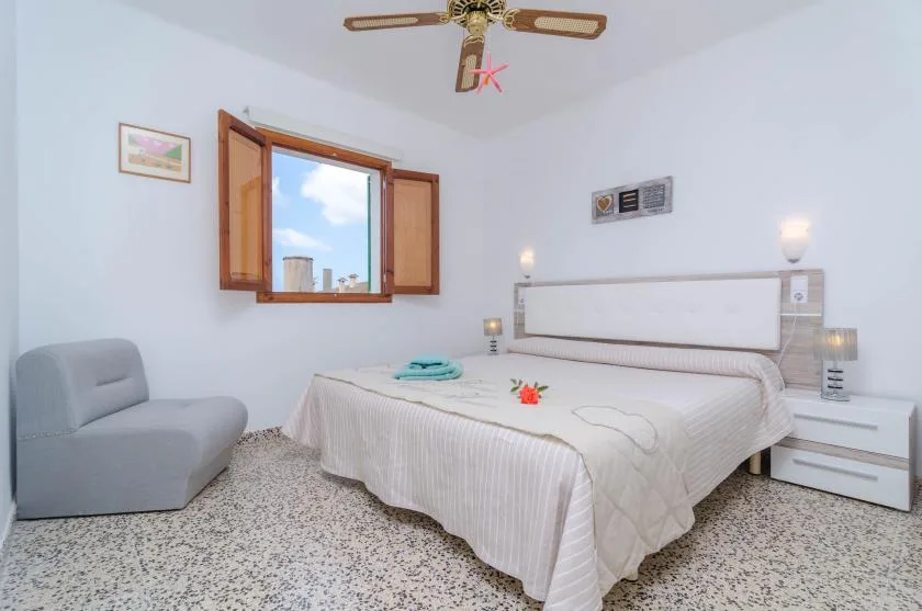 A bedroom with a bed, a gray seat, and an open window.