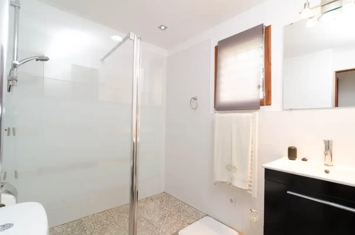 A bright bathroom with a glass shower and a dark vanity.