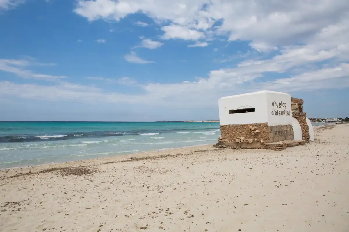 A sandy beach with turquoise water and a small white structure.