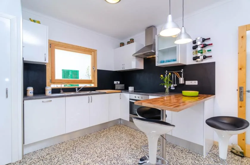 A bright kitchen with white cabinets, a dark backsplash, and a wood-topped counter.