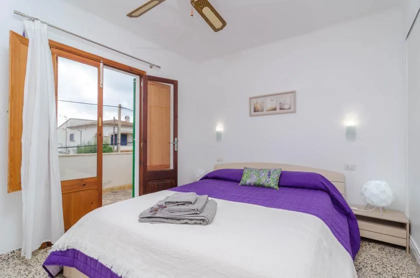 A bedroom with a bed dressed in white and purple bedding beside a glass door.