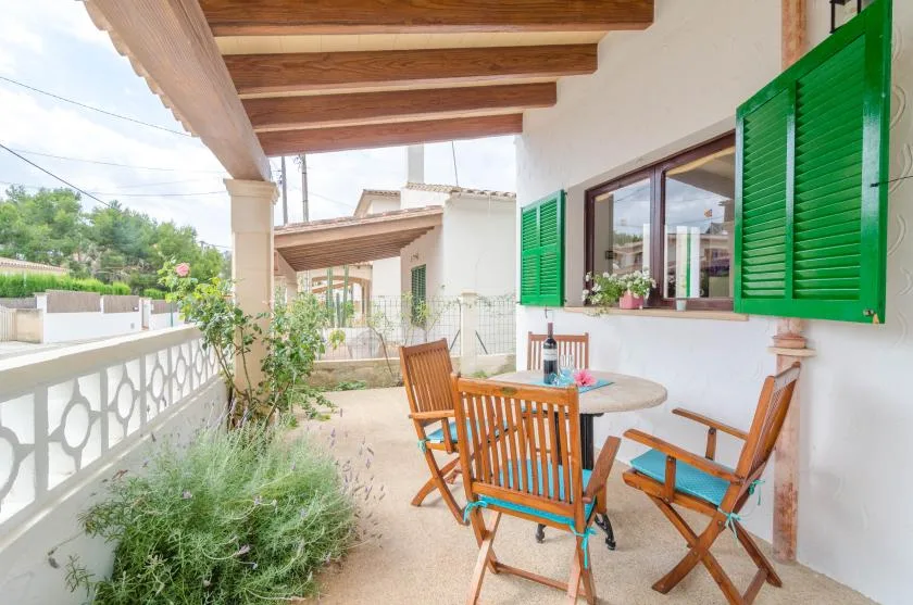 A covered outdoor terrace with a wooden table and seating beside green shutters.