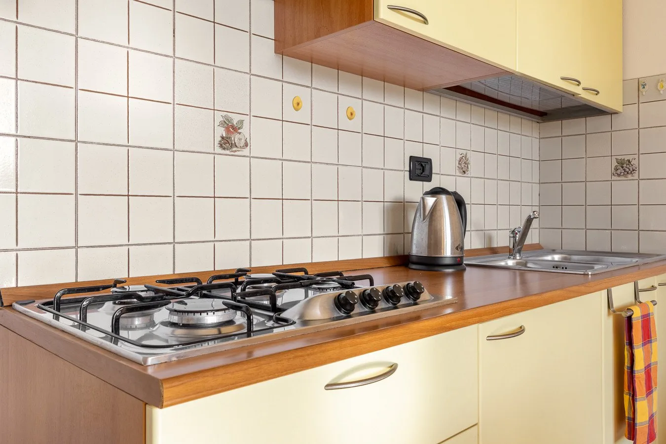 Una encimera de cocina con azulejos, una estufa de gas, una tetera y un fregadero.