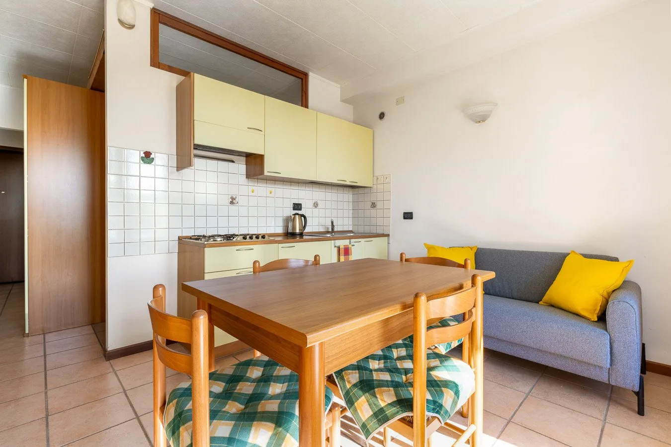 Comedor con una mesa de madera junto a una cocina pequeña y un sofá.