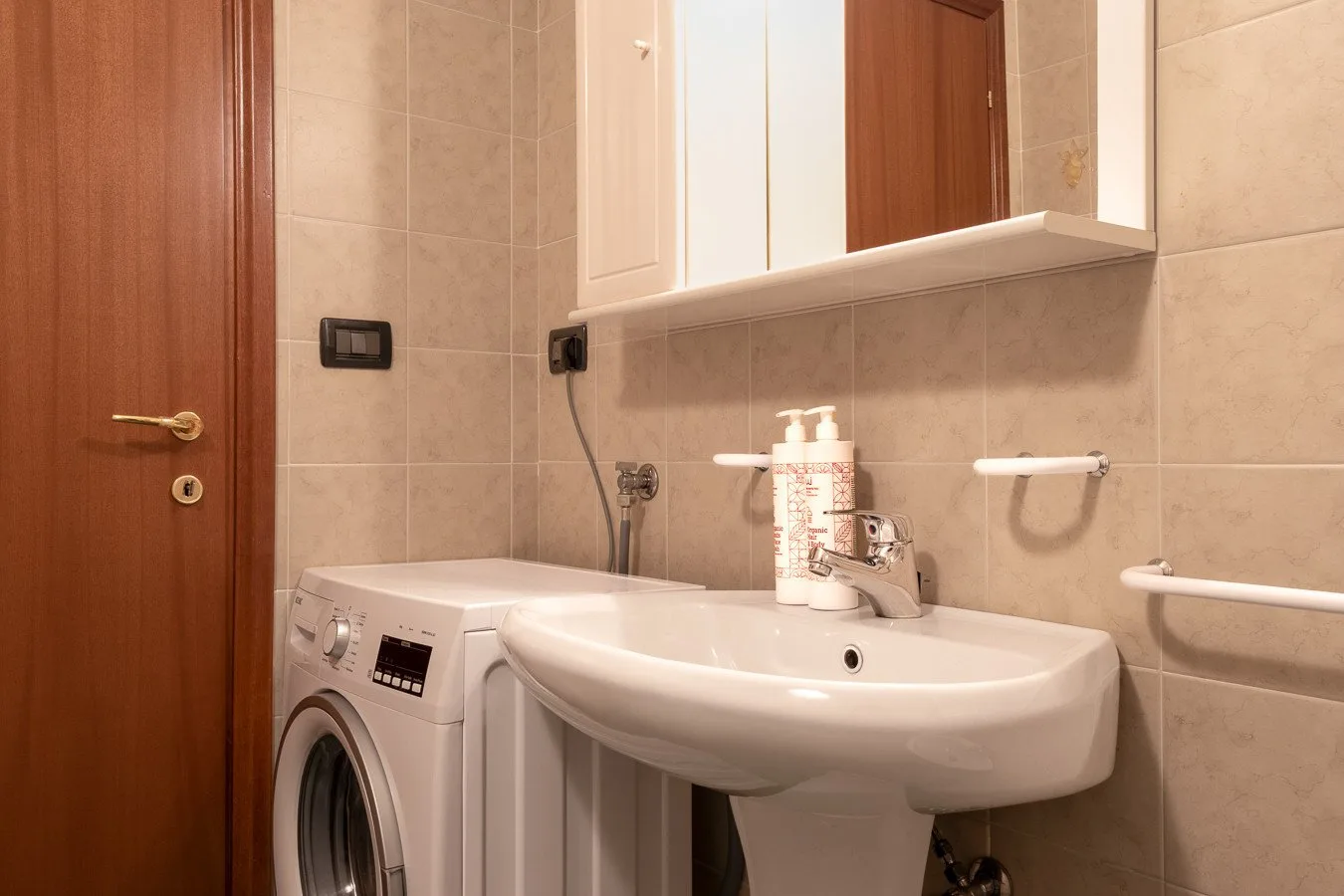 Un baño alicatado con lavabo, lavadora y espejo de pared.