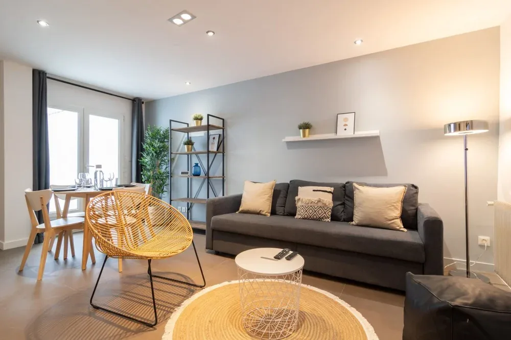 A modern living room with a dark sofa and a small dining area by the windows.