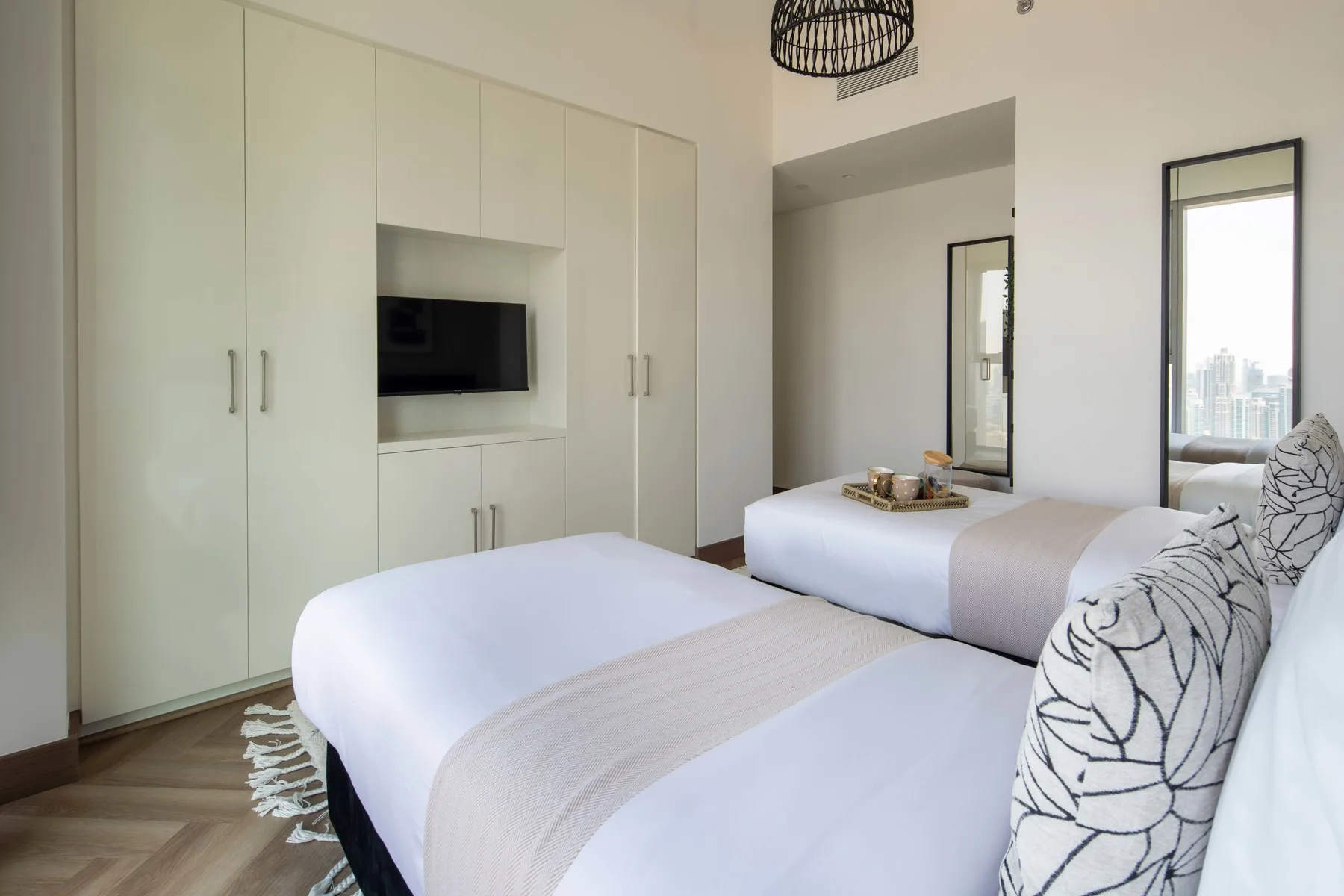 Un dormitorio luminoso con dos camas, armarios empotrados y un televisor en la pared.