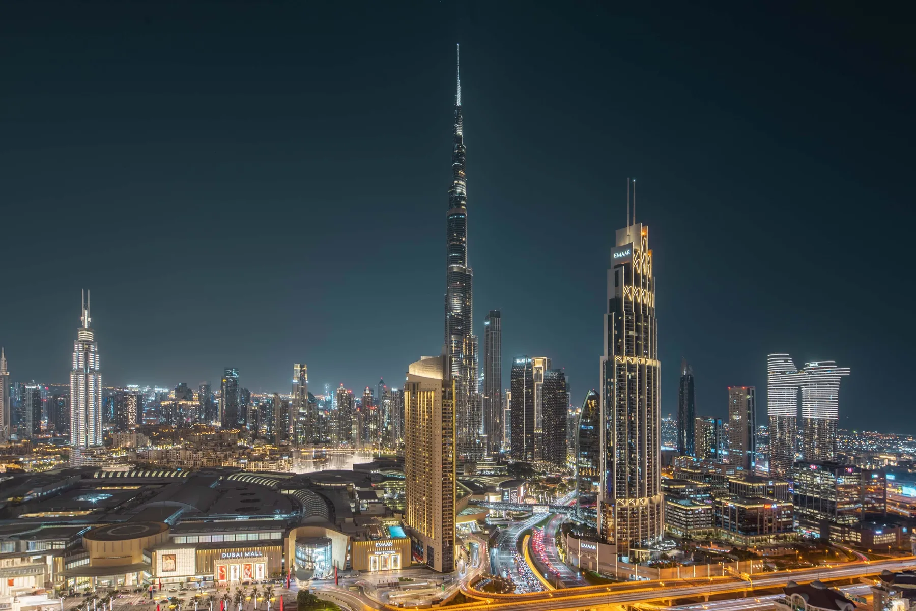 Horizonte urbano nocturno con el Burj Khalifa iluminado sobre los edificios cercanos.