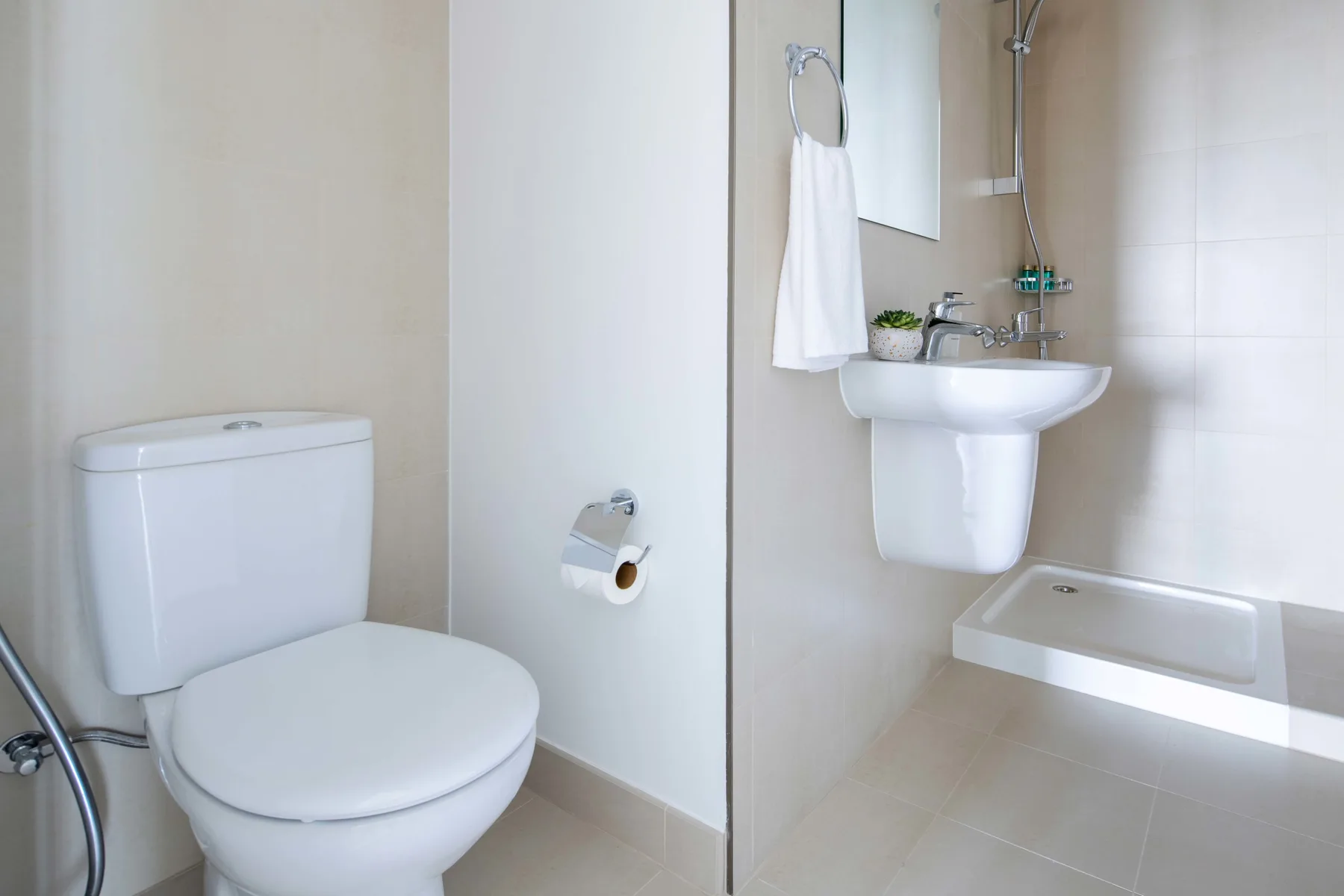 Un baño luminoso con inodoro, lavabo de pared y ducha.