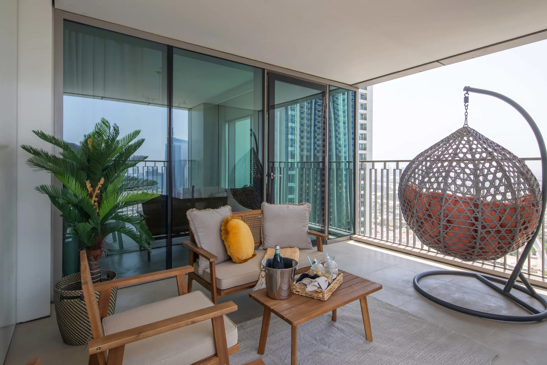 Un espacio de estar en el balcón con una silla colgante y una mesa pequeña.