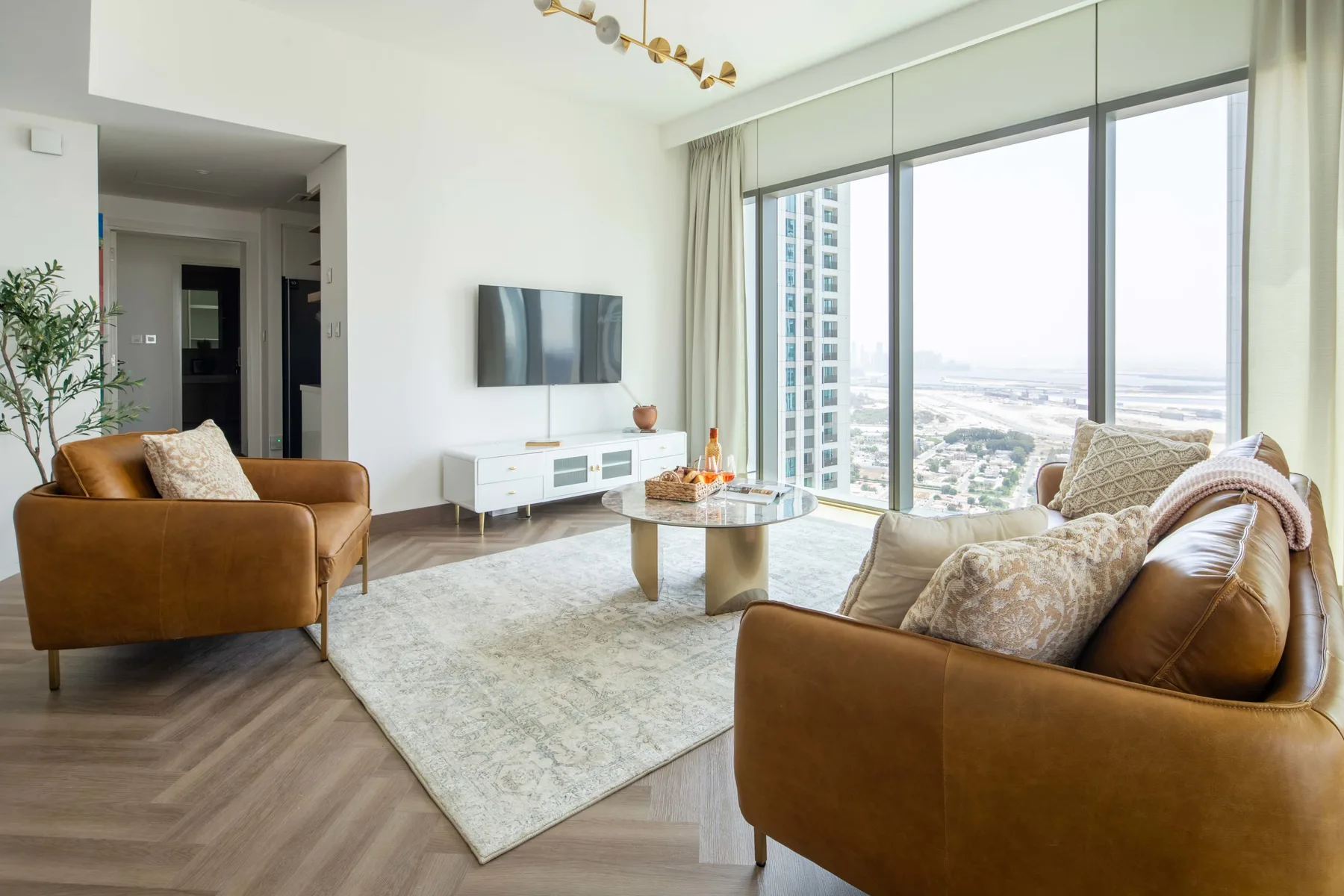 Una sala luminosa con asientos marrones, un televisor y grandes ventanas.