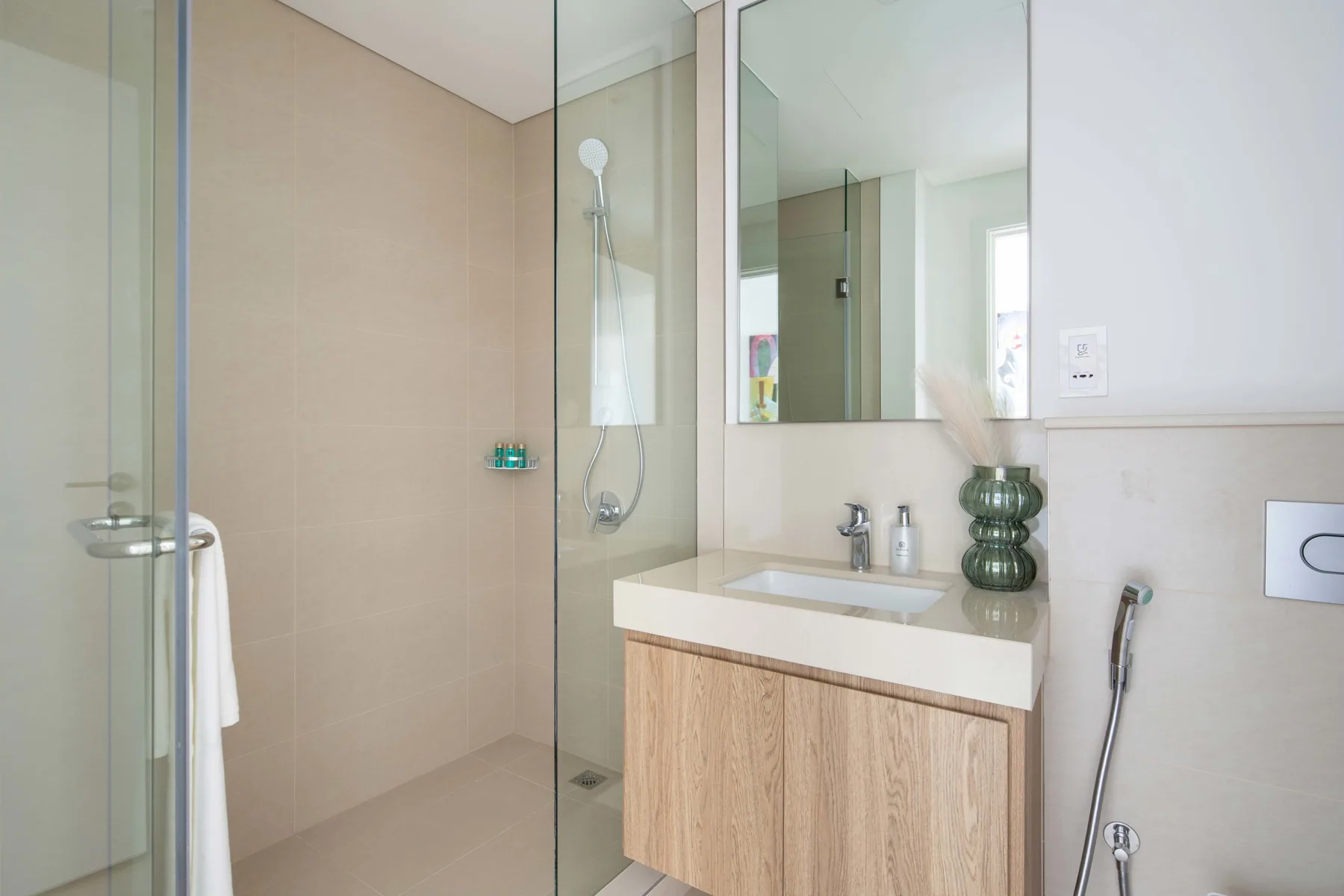 Un baño luminoso con una ducha de vidrio y un lavabo con mueble de madera.